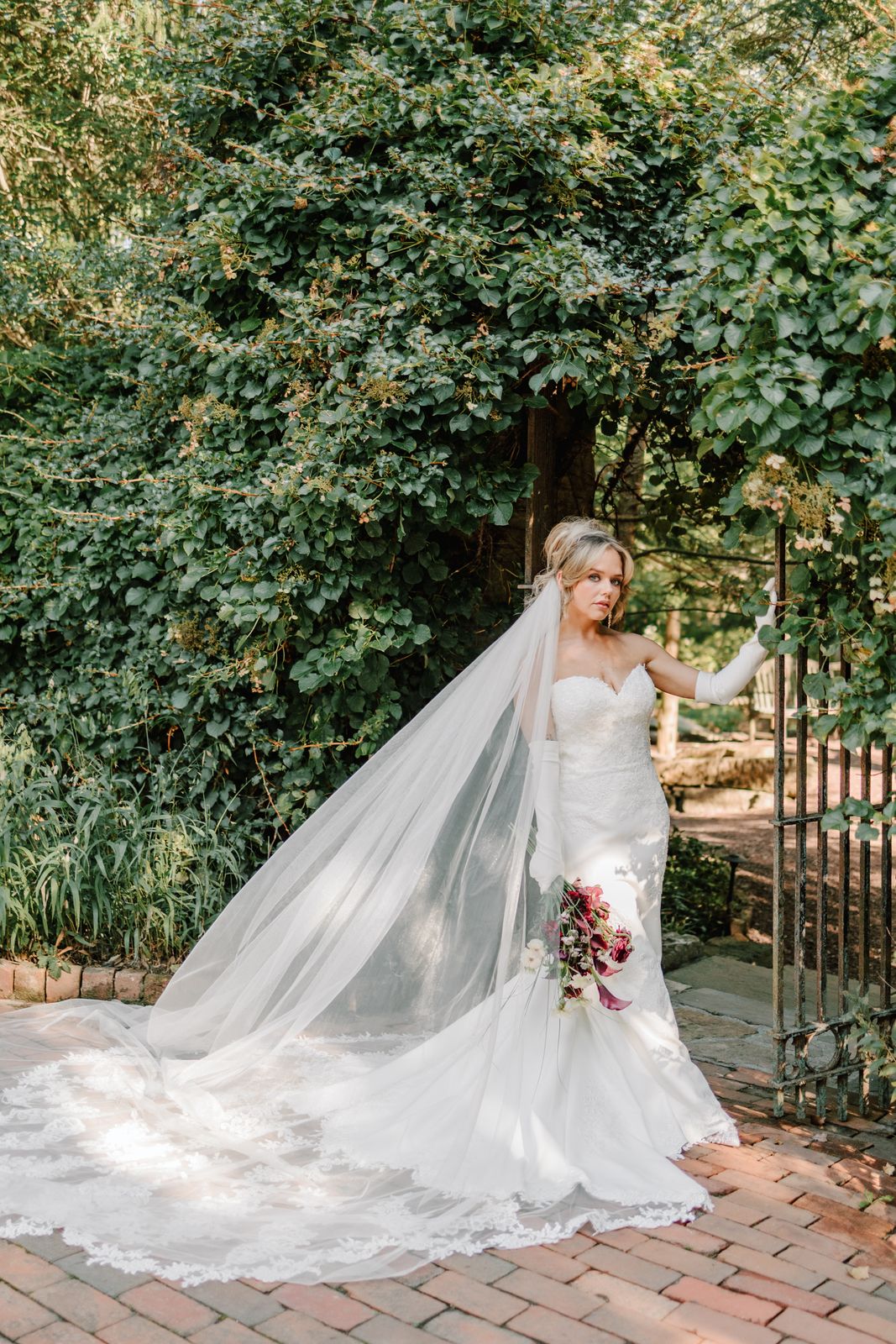 MacKenzie in her wedding gown and long veil at a garden gate