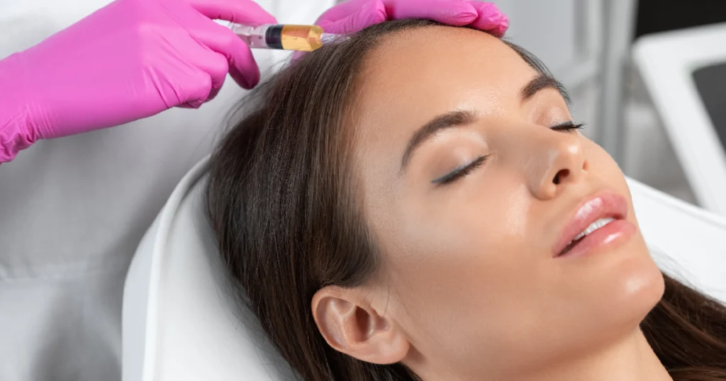 Woman receiving PRP hair restoration treatment with a syringe injected into the scalp by a professional wearing pink gloves in Hamilton, NJ