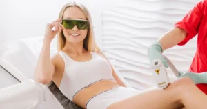 A smiling woman with protective glasses receiving laser hair removal on her leg in Cranston, RI